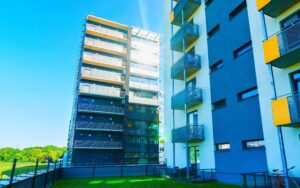 Apartment in residential building exterior. Housing structure at blue modern house of Europe. Rental home in city district on summer. Wall and glass high architecture for business property investment.