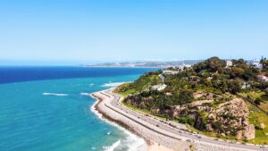 Aerial drone view of Tangier, Morocco. Strait of Gibraltar coastline, rocky hills with residential buildings and greenery, highway with moving cars